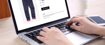 People buying blue navy jeans on ecommerce website with smart phone, credit card and coffee on wooden desk